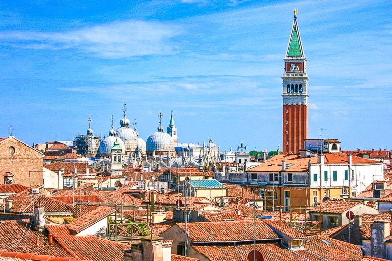 red clock tower over orange rooftops one day in venice italy
