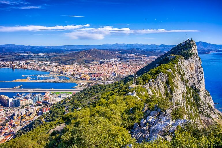 Hoher Felsen mit grünen Sträuchern und Stadt in der Ferne Gibraltar