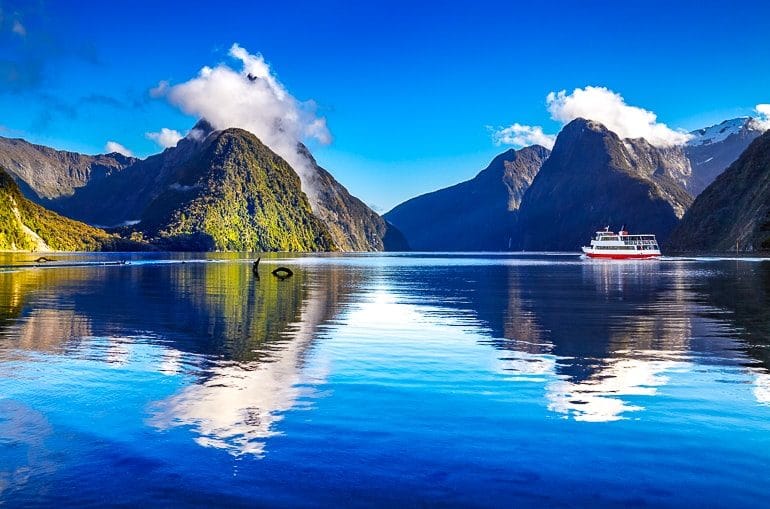 blue water with tour boat and towering cliffs behind milford sound