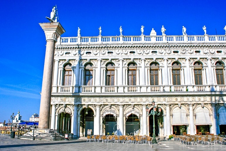 Weißes verzierters Gebäude mit blauem Himmel und Stühlen im Vordergrund Markusplatz Venedig