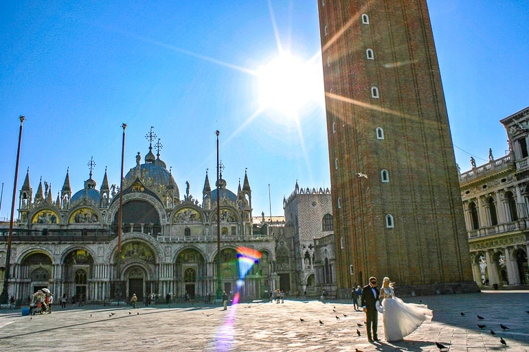 couple walking through square with tower and sun behind st marks square things to do in venice italy