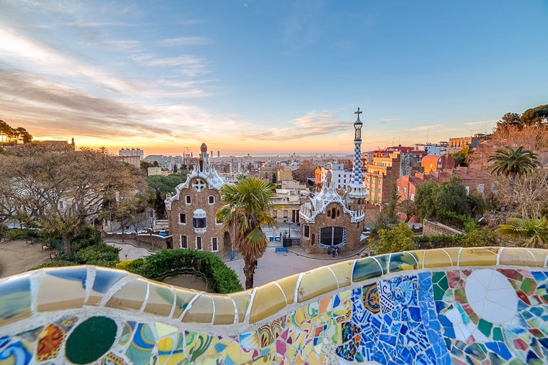 colourful tiles of bench with coloured houses below and sunset guell park barcelona