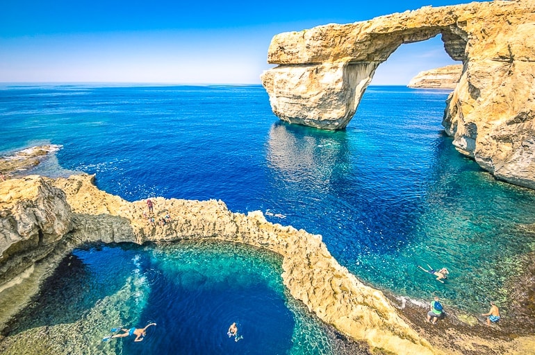 Blaues Meer mit Felsbogen und Schwimmern vor der Küste von Gozo