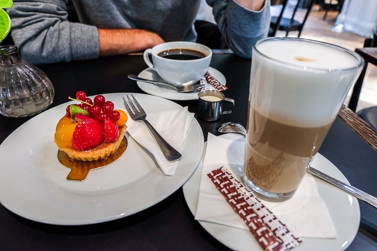Obsttörtchen mit Tasse und Glas Kaffee auf schwarzem Tisch Cafe Luitpold München