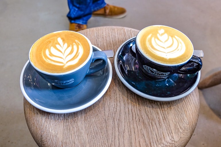 Zwei Tassen mit Kaffee auf Holzhocker mit Schuhen im Hintergrund München Cafés