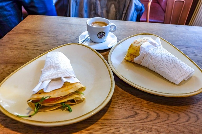 Zwei Crepes eingewickelt in Papier auf Tellern mit Kaffeetasse auf Tisch