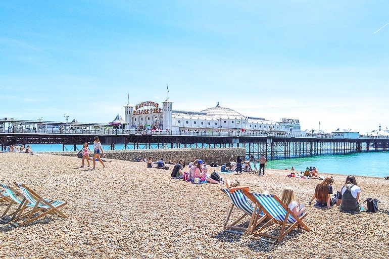 long ocean pier with white building and rock beach in front in brighton day trip from london