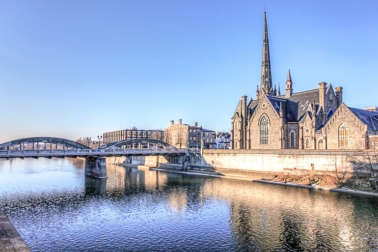 Kirche aus Stein mit Turm entlang blauem Fluss mit Brücke Cambridge Ontario