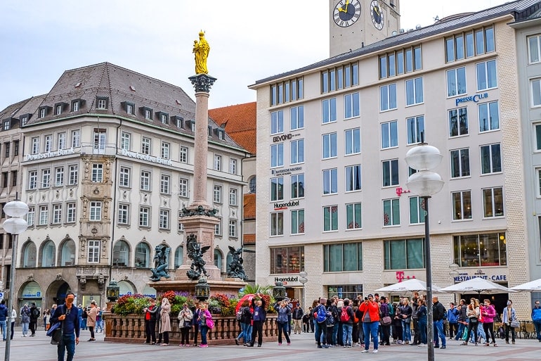 hotel buildings behind people standing in market square with golden statue in front.