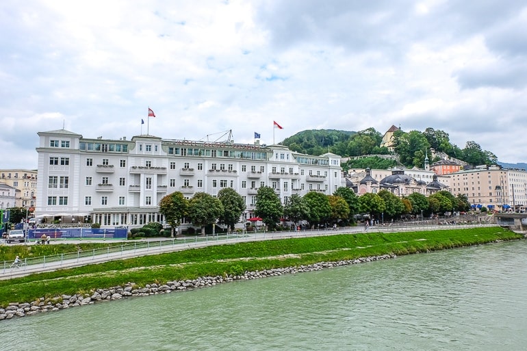 Weißes Hotel in Stadt an Flussufer mit Fluss im Vordergrund in Salzburg.