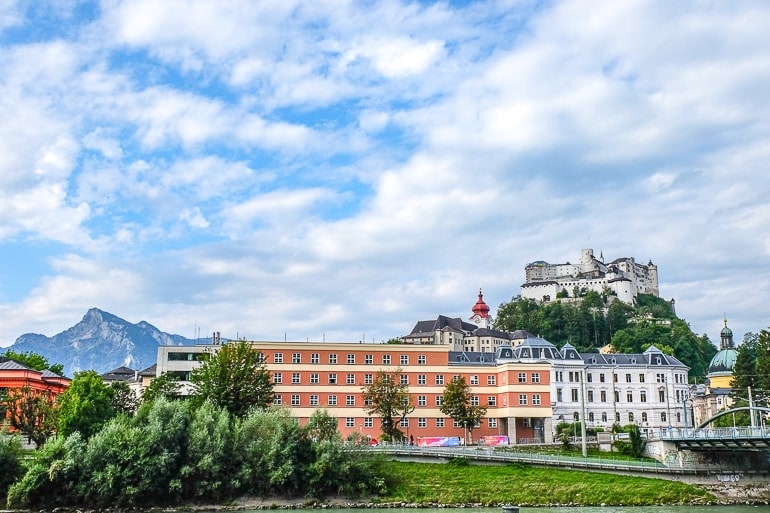 Festung auf grünem Hügel über Gebäuden in Altstadt von Salzburg.