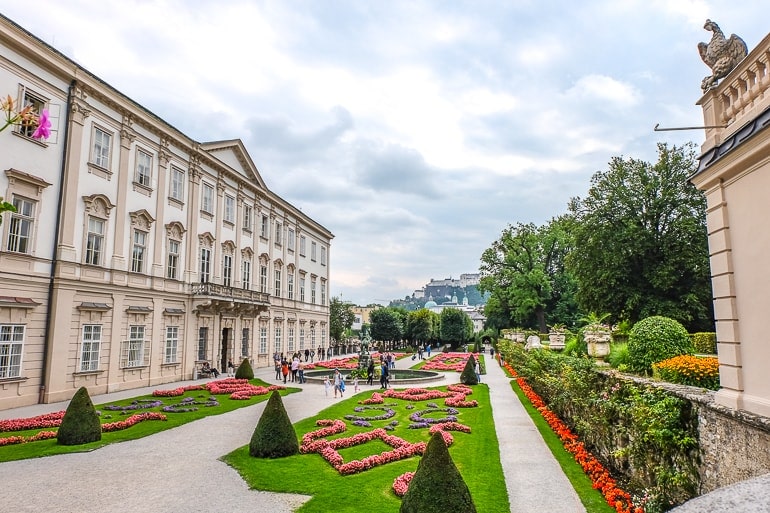 Garten mit Gras, Blumen, Gehwegen und historischen Gebäuden Schloss Mirabell Salzburg.
