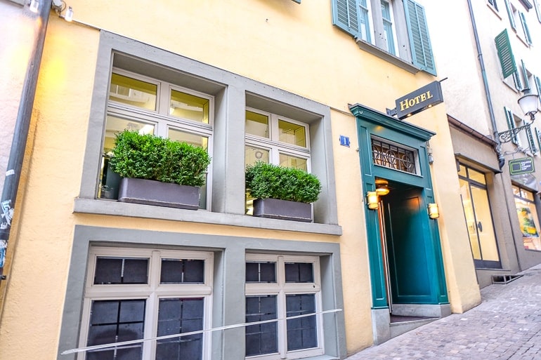 yellow hotel with green door along cobblestone road in old town zurich.