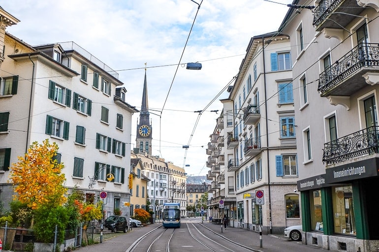 busy street with shops and tram with church clock tower behind in zurich.