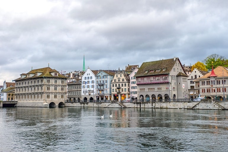 old town buildings and rathaus along river with cloudy sky above.