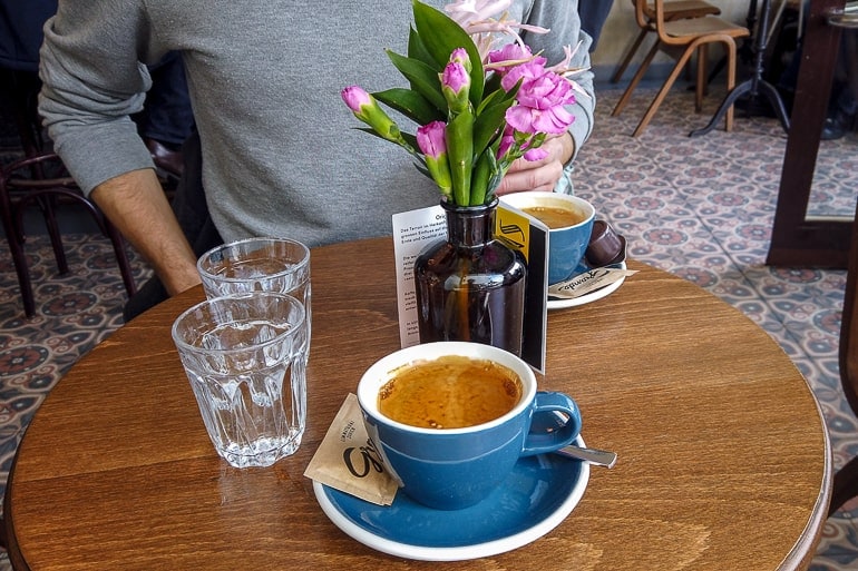 coffees in blue mugs on wooden cafe table with flowers