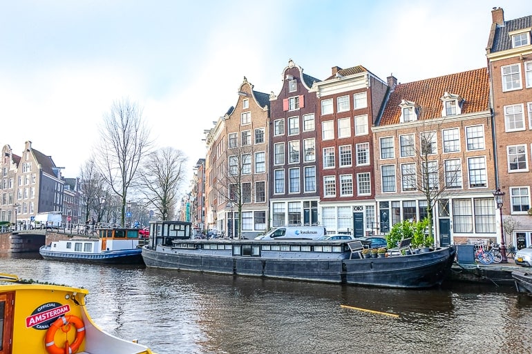 Schwarzes Hausboot auf Gracht in Amsterdam mit Häusern im Hintergrund
