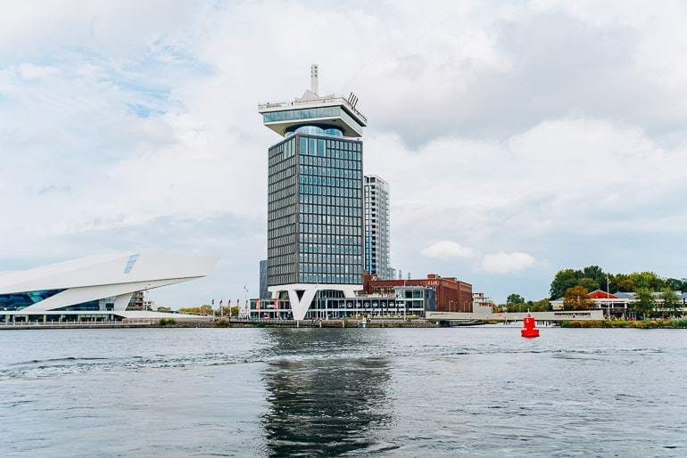 tall glass tower standing by river edge in amsterdam