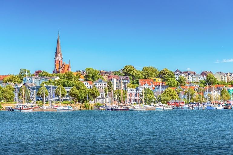 church up on hill with houses below and shoreline in front flensburg germany