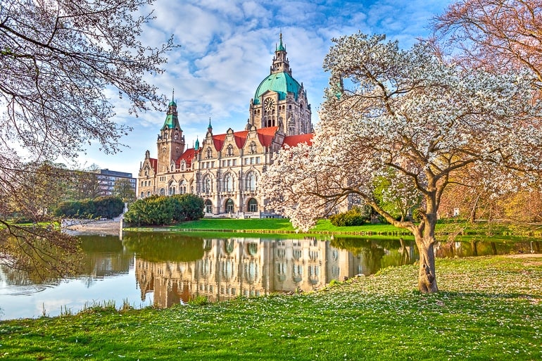 large building with dome behind blooming trees in park with water beside hanover germany