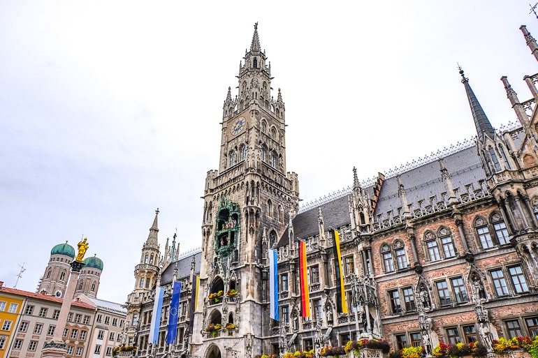 Hoher verzierter Turm als Teil des Neuen Rathauses mit Flaggen davor Marienplatz München