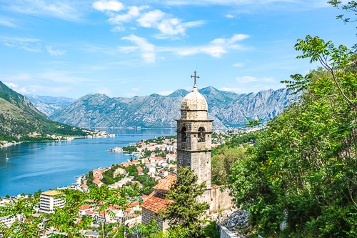 old stone tower on hillside with old town and blue bay below in kotor montenegro