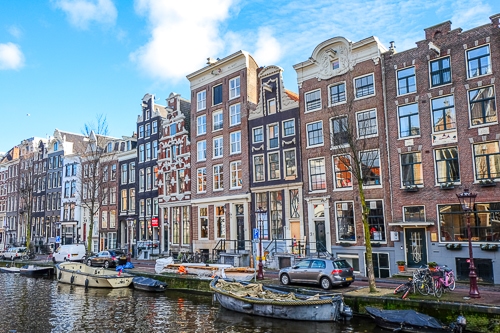 Schmale Gebäude aus Stein mit Fenstern und Kanal mit kleinen Booten davor in Amsterdam