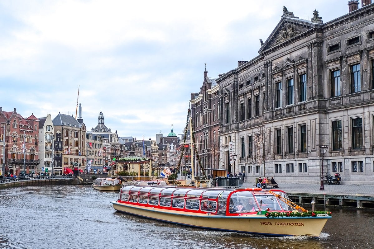 Flaches Kanalboot auf Wasser im Stadtzentrum von Amsterdam mit Häusern im Hintergrund.