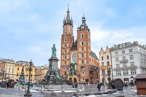 Kirche mit zwei Kirchtürmen und Statue davor auf Marktplatz in Krakau mit blauem Himmel
