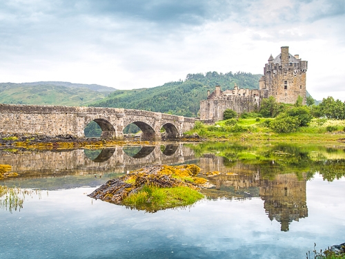 steinerne Burg mit Steinbrücke und Wasser drum herum in Schottland.