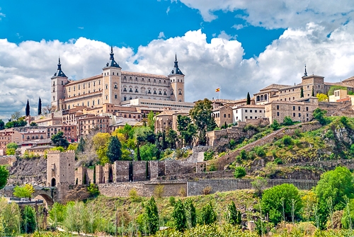 large fortress with towers on hillside wit blue sky and houses beside in spain