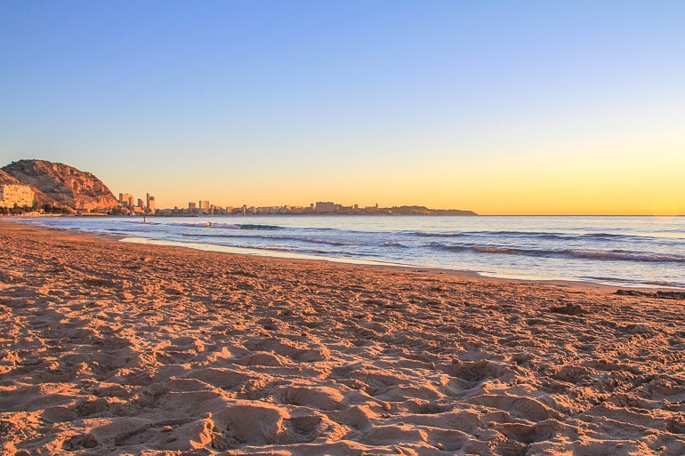 Sandiger Strand mit Hügel im Hintergrund bei Sonnenuntergang