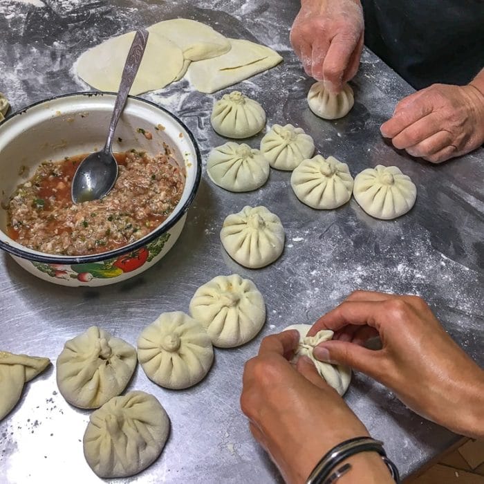 hands making dumplings on metal table with bowl beside