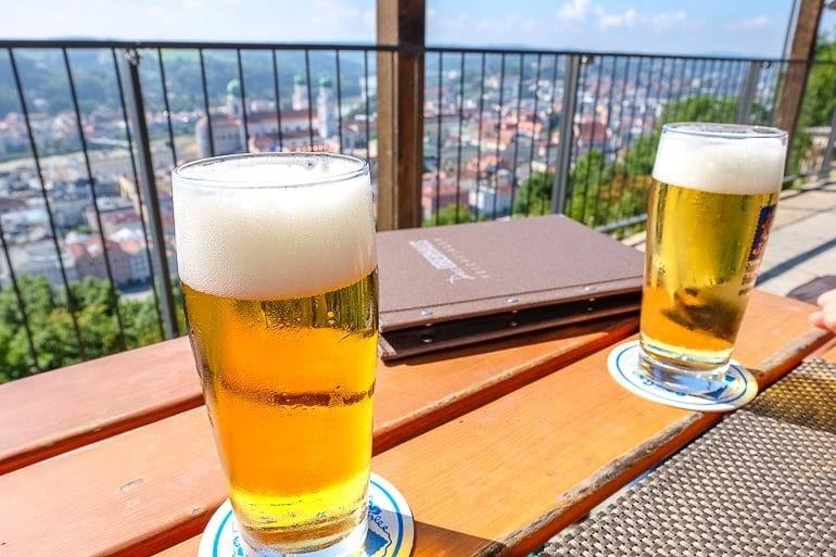 two beer pint glasses on wooden table overlooking city.