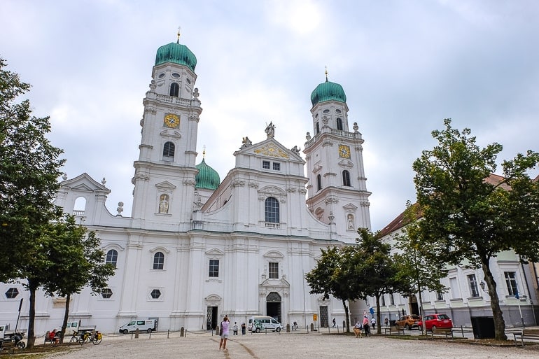 white cathedral entrance with green domed towers and open square in front.