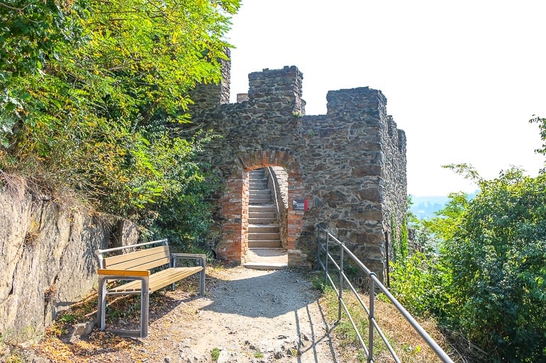 Steinmauer mit Eingang und Parkbank entlang eines Pfades