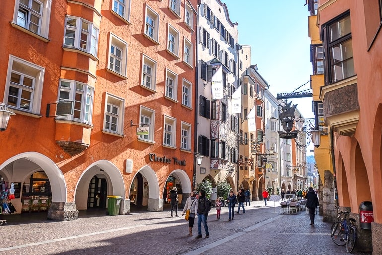Menschen laufen neben orangenem Gebäude in Altstadt von Innsbruck