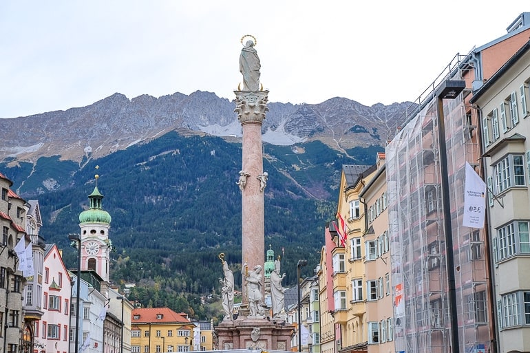 stone pillar column in middle of shopping street with statue above and mountains behind.