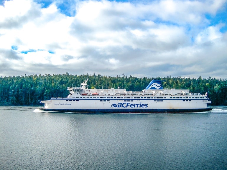 large ferry sailing in water with green trees behind and cloudy sky above.