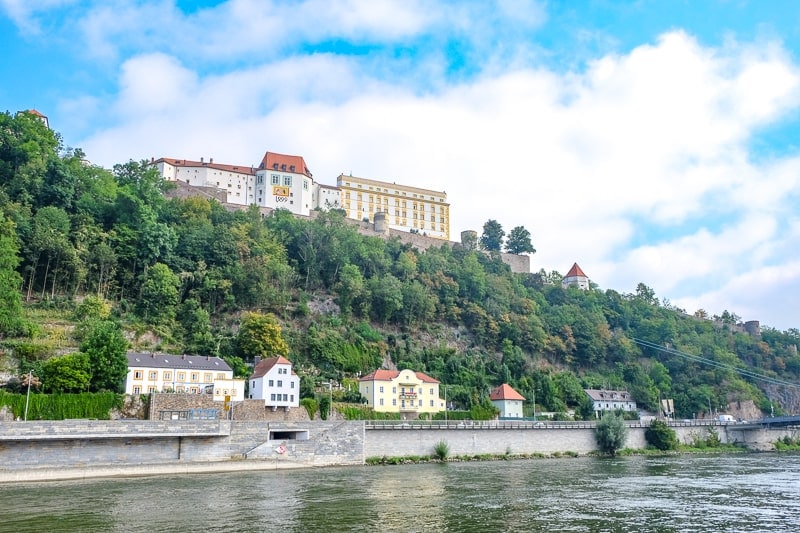 large castle up on green hillside with river below in passau