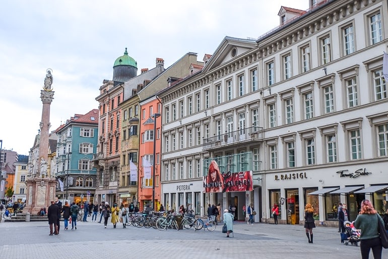 Menschen laufen entlang Straße mit bunten Läden und Statue in Innsbruck