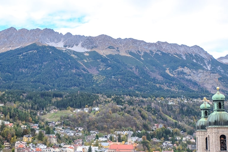 large mountain with green trees and rocky top with old town down below