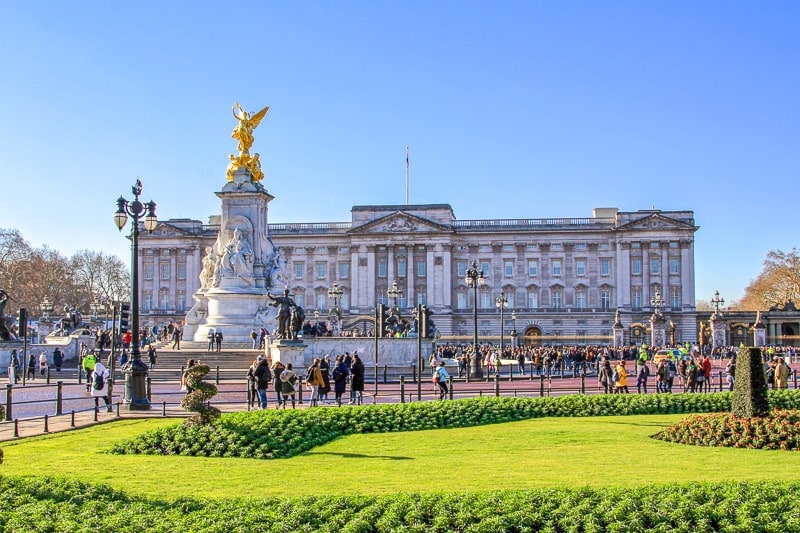 large buckingham palace with statue in front and people crowding the main gate in london