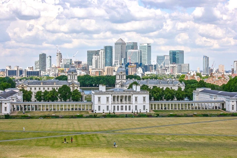 tall buildings of canary wharf london with green lawn of greenwich in front