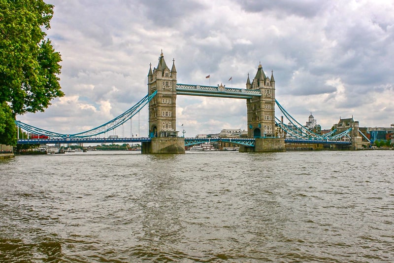 large bridge with two towers over rover thames with cloudy sky above.