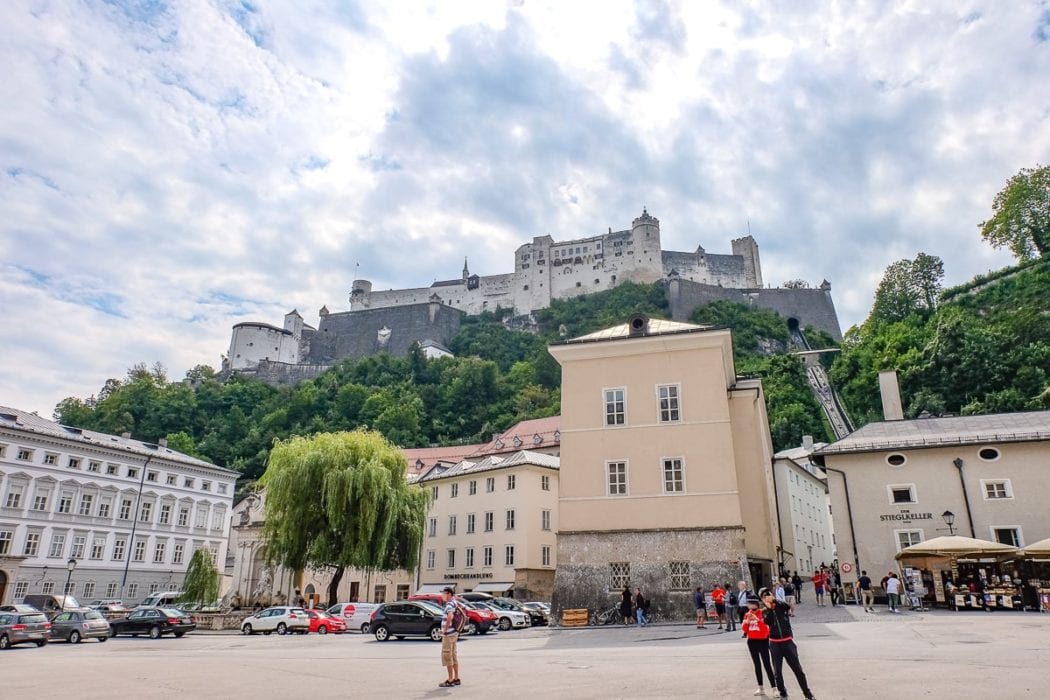 castle on hill with buildings and people below in salzburg