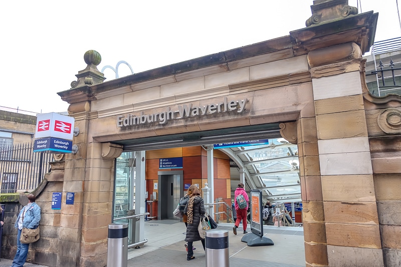 stone entrance to train station in edinburgh with people standing in front.