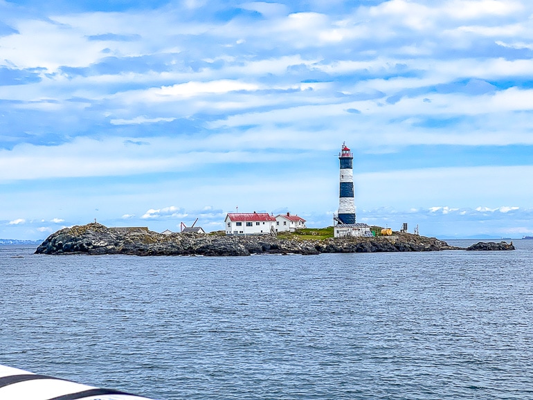 rocky island with striped lighthouse with ocean in front and blue sky above.