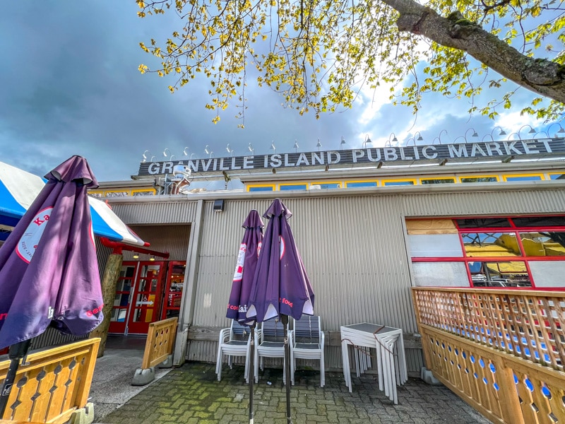 sign above building for granville island public market with folded umbrellas in front.