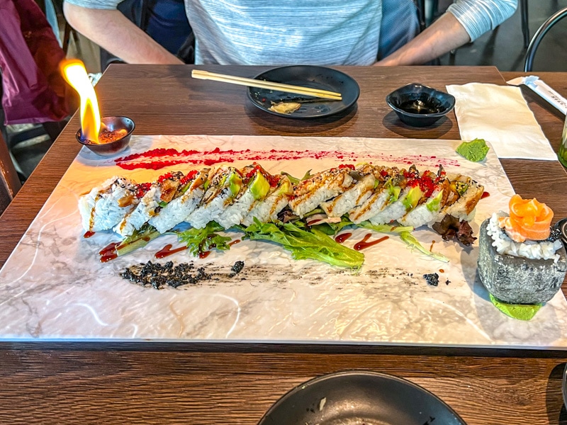 fancy sushi roll on white platter on wooden table with chopsticks and candle around.